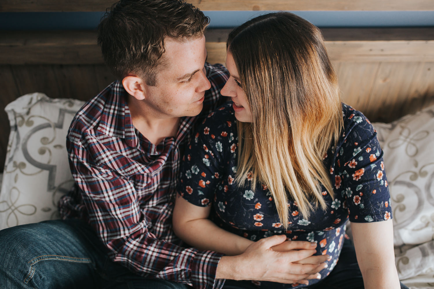 expecting couple snuggles on bed, hands holding wife's pregnant belly - Stouffville In-Home Photography