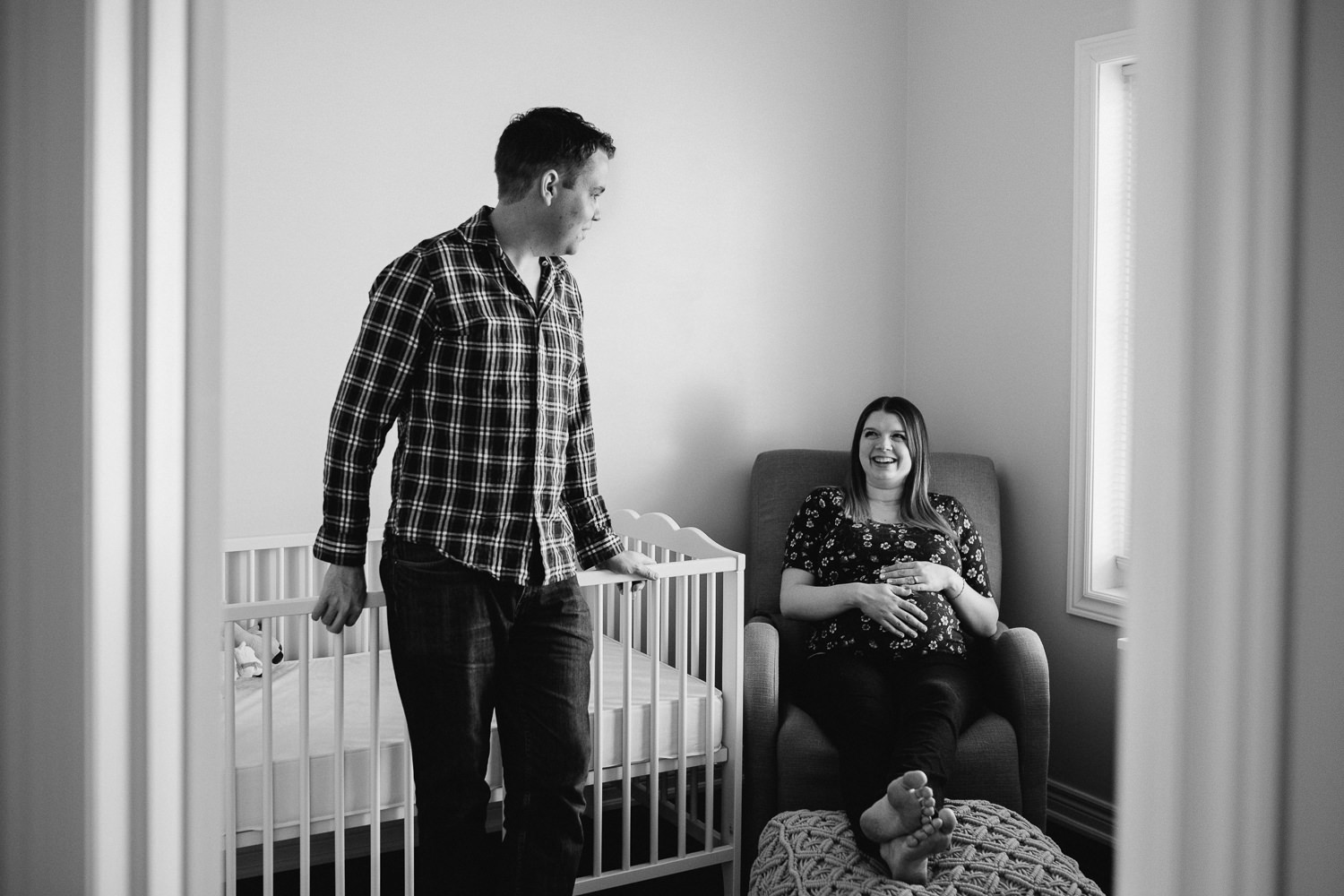pregnant mom sits in nursery glider smiling at husband, hands on baby belly - Uxbridge In-Home Photography