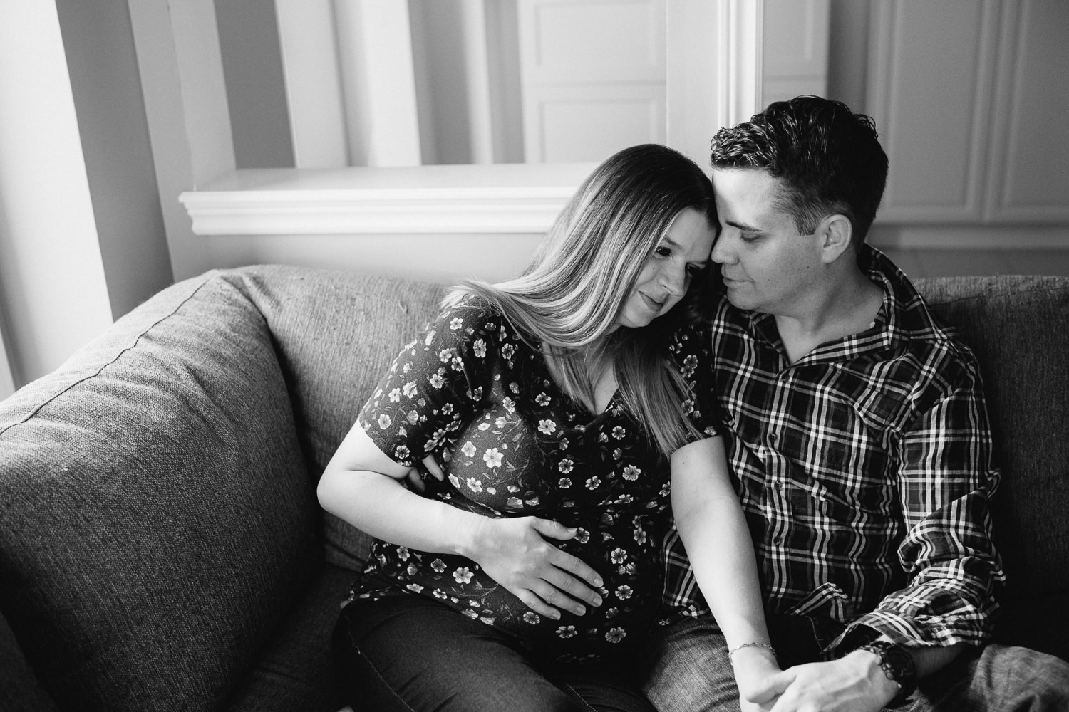 expecting couple snuggles on couch, pregnant mom holding baby belly - Newmarket Lifestyle Photography