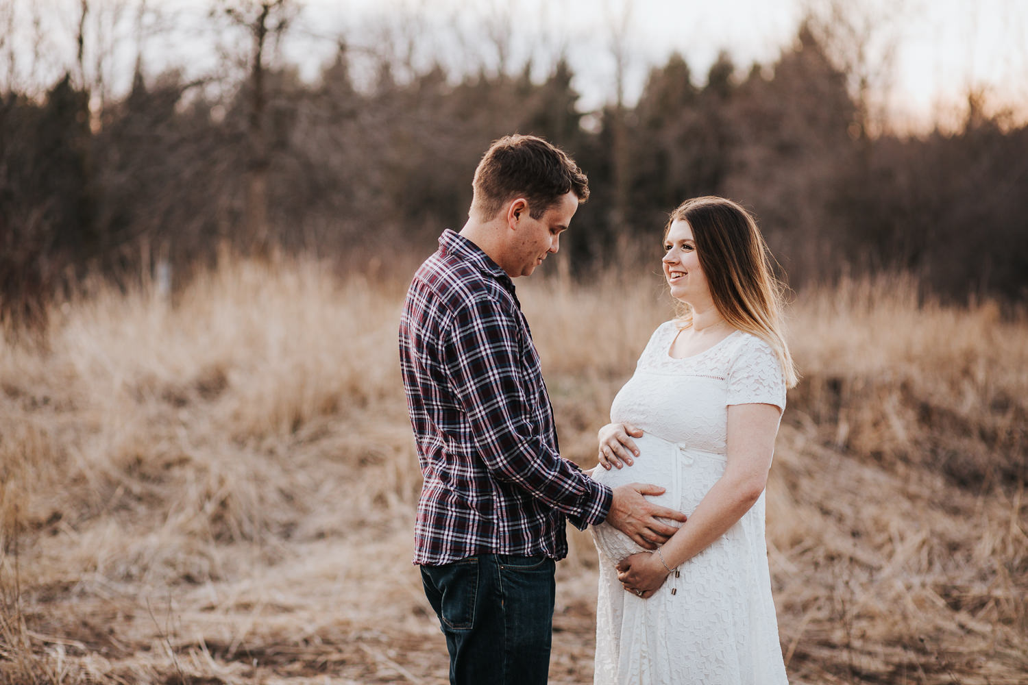 husband and pregnant wife standing in field, holding baby belly - Newmarket Sunset Photos