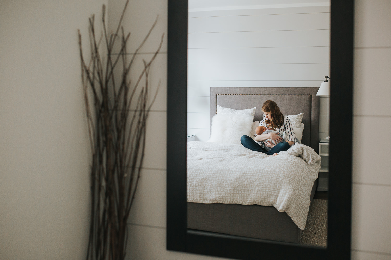 new mom sitting on bed holding 2 week old baby boy wrapped in blanket, mirror reflection - Stouffville Lifestyle Photography