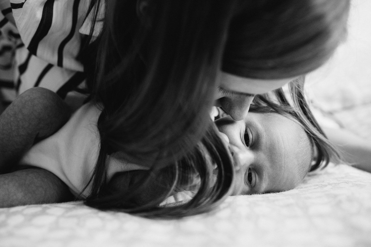 first time mother kisses 2 week old baby son's forehead as he lies on bed - Markham Lifestyle Photography