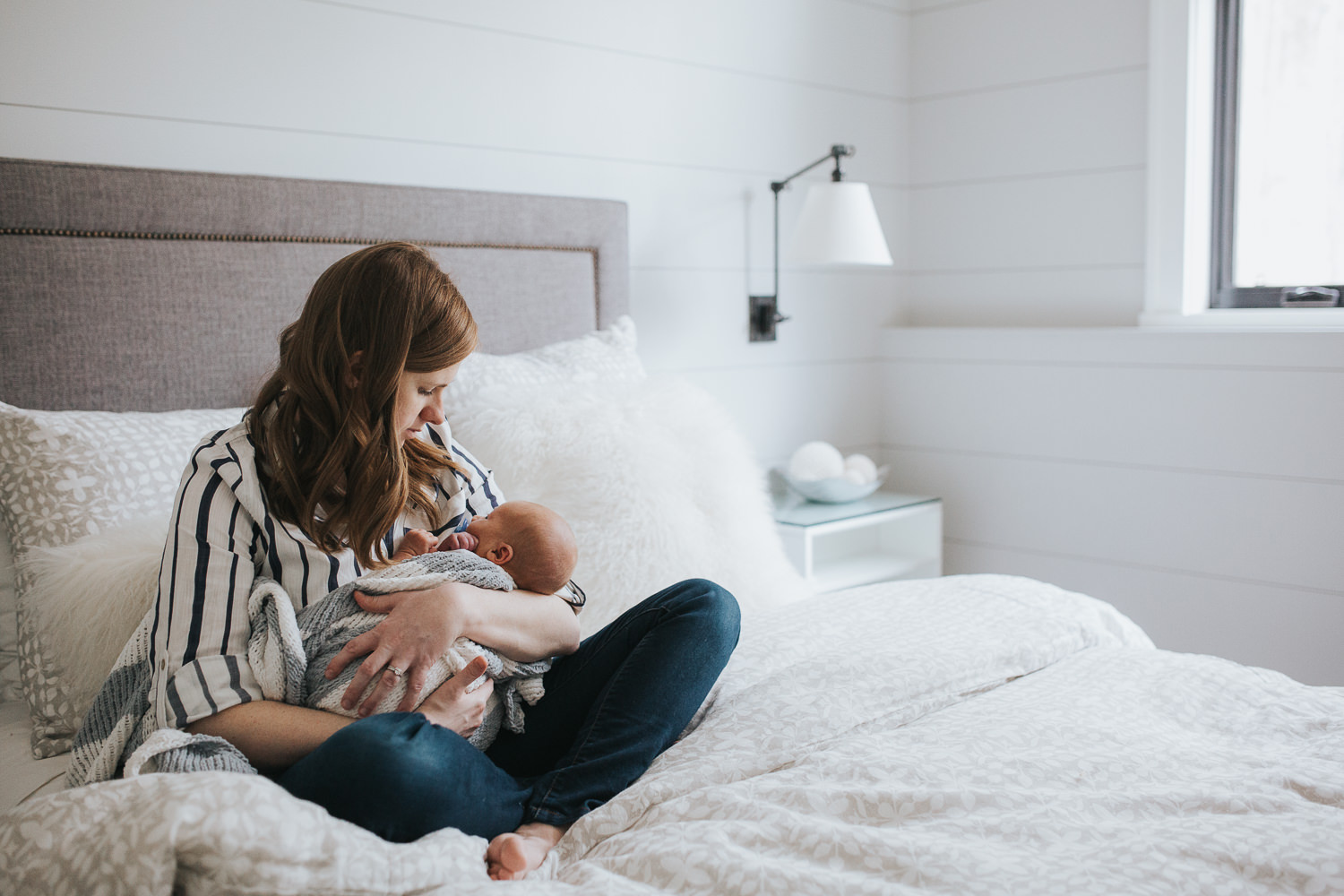 new mom sitting on bed holding 2 week old baby boy wrapped in blanket -  Newmarket Lifestyle Photography