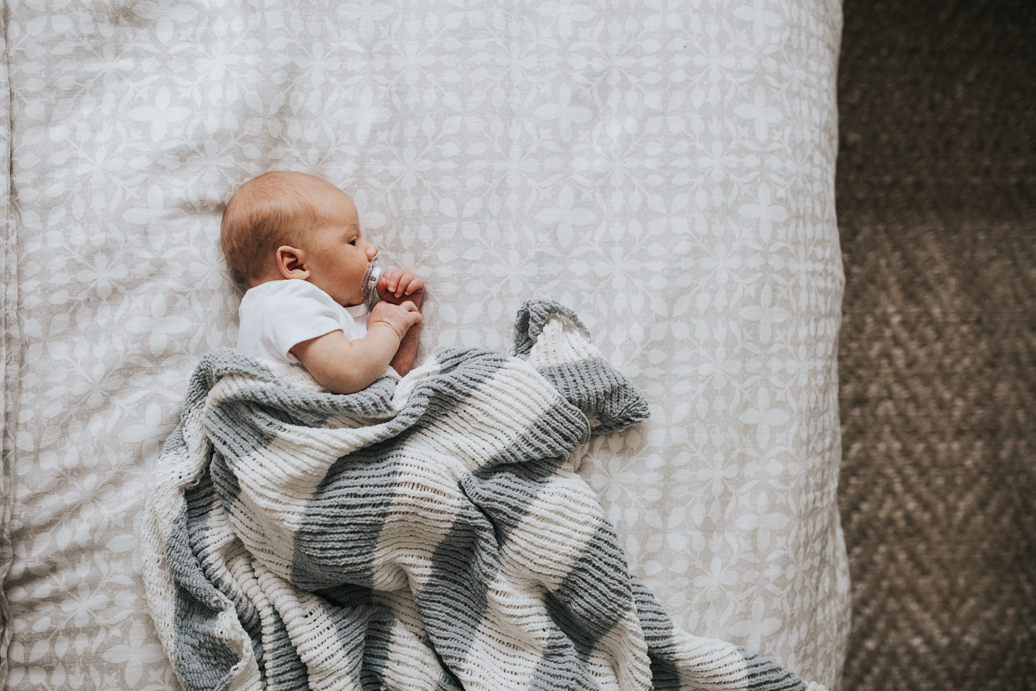 two week old baby boy lying on bed under hand knitted blanket - Stouffville In-Home Photography