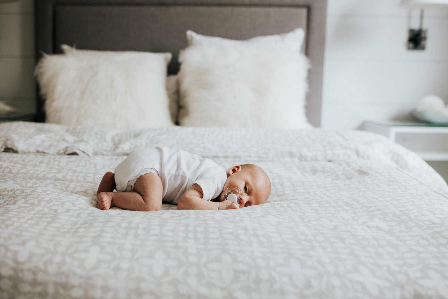 two week old baby boy lying on tummy on bed wearing white onesie - Markham In-Home Photography