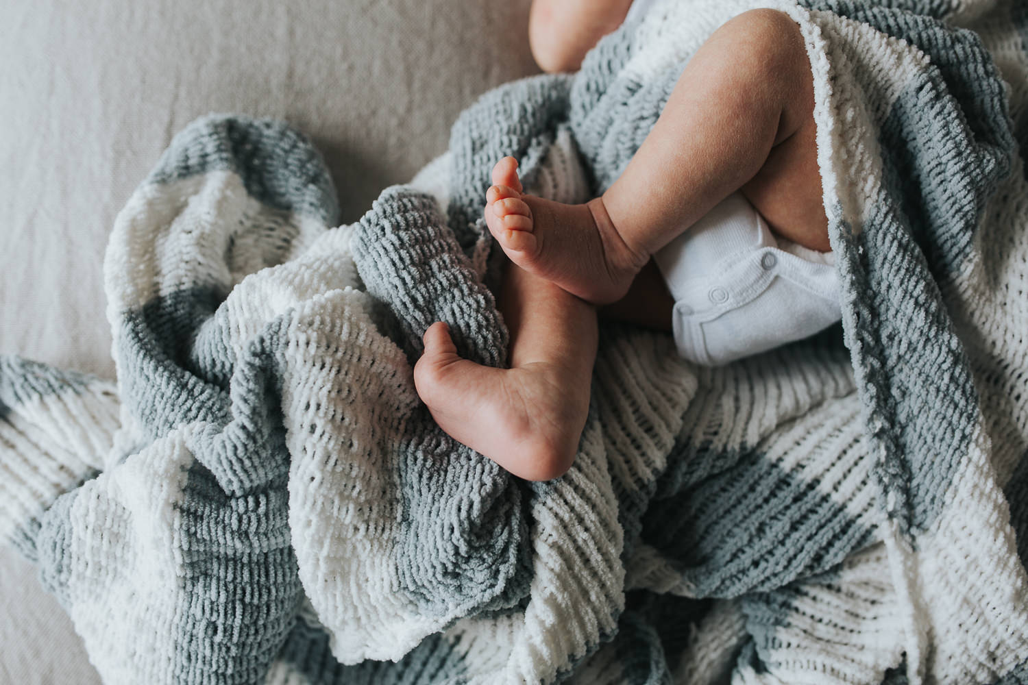 two week old baby boy lying on bed under hand knitted blanket, close up of feet - Markham Lifestyle Photos