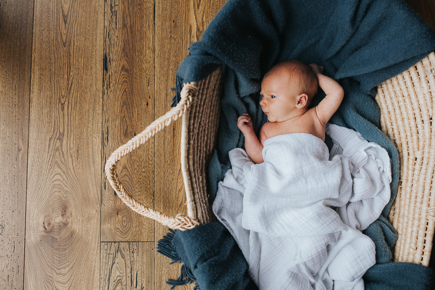 2 week old baby boy lying with arms by face in Moses basket - Markham Lifestyle Photography