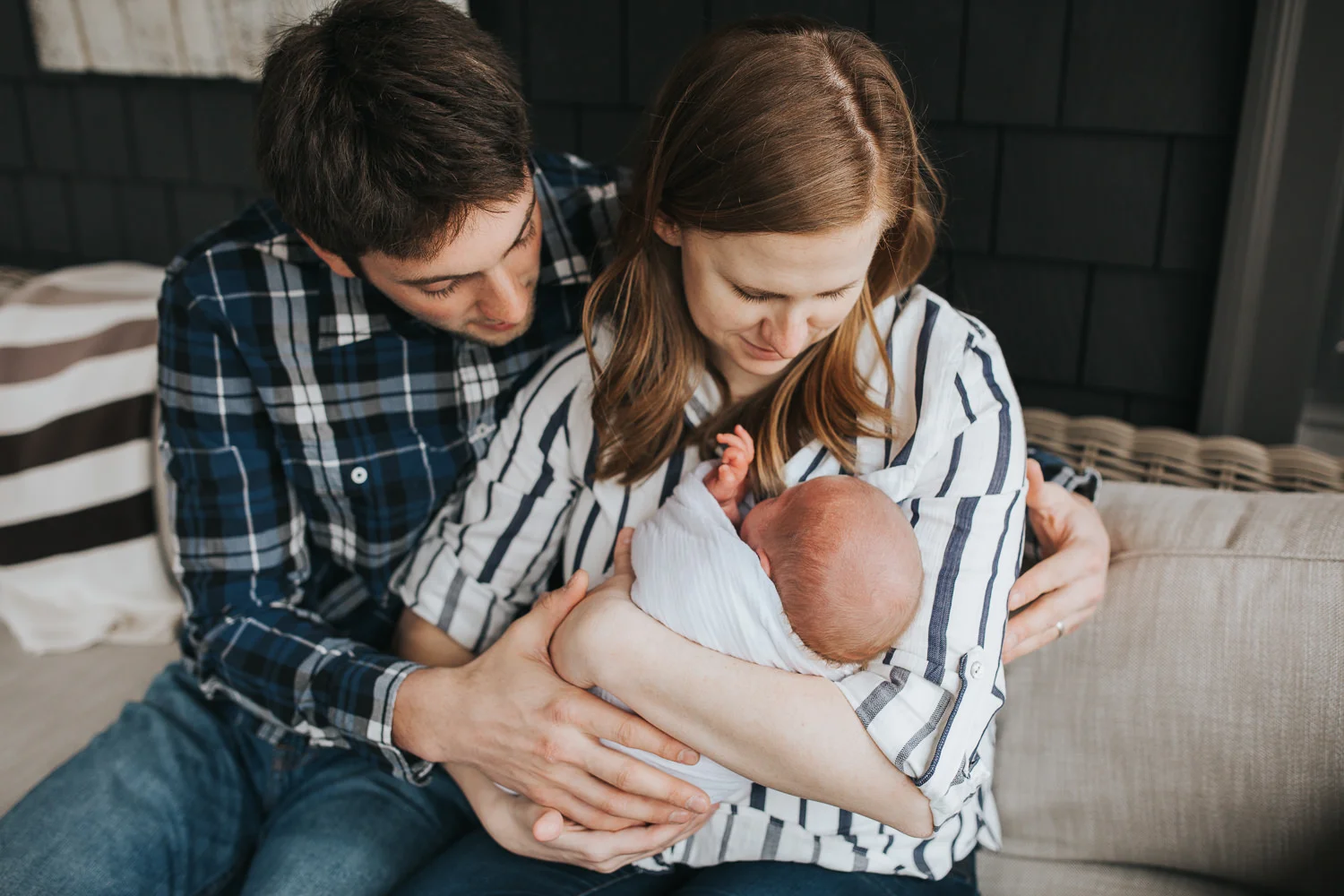 first time parents sitting on couch holding and looking at 2 week old baby boy - Stouffville In-Home Photography