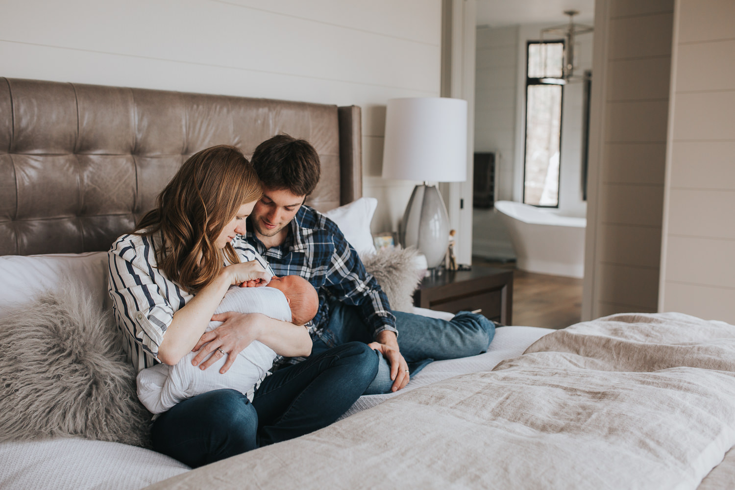 first time parents sitting on bed holding and looking at 2 week old baby boy - Markham In-Home Photography