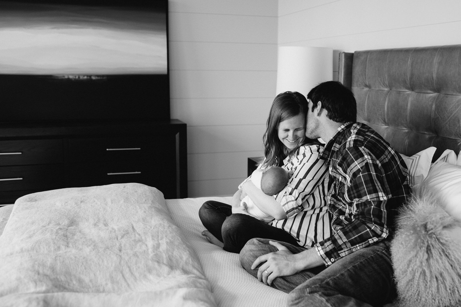 first time parents sitting on bed holding and looking at 2 week old baby boy - Barrie In-Home Photography