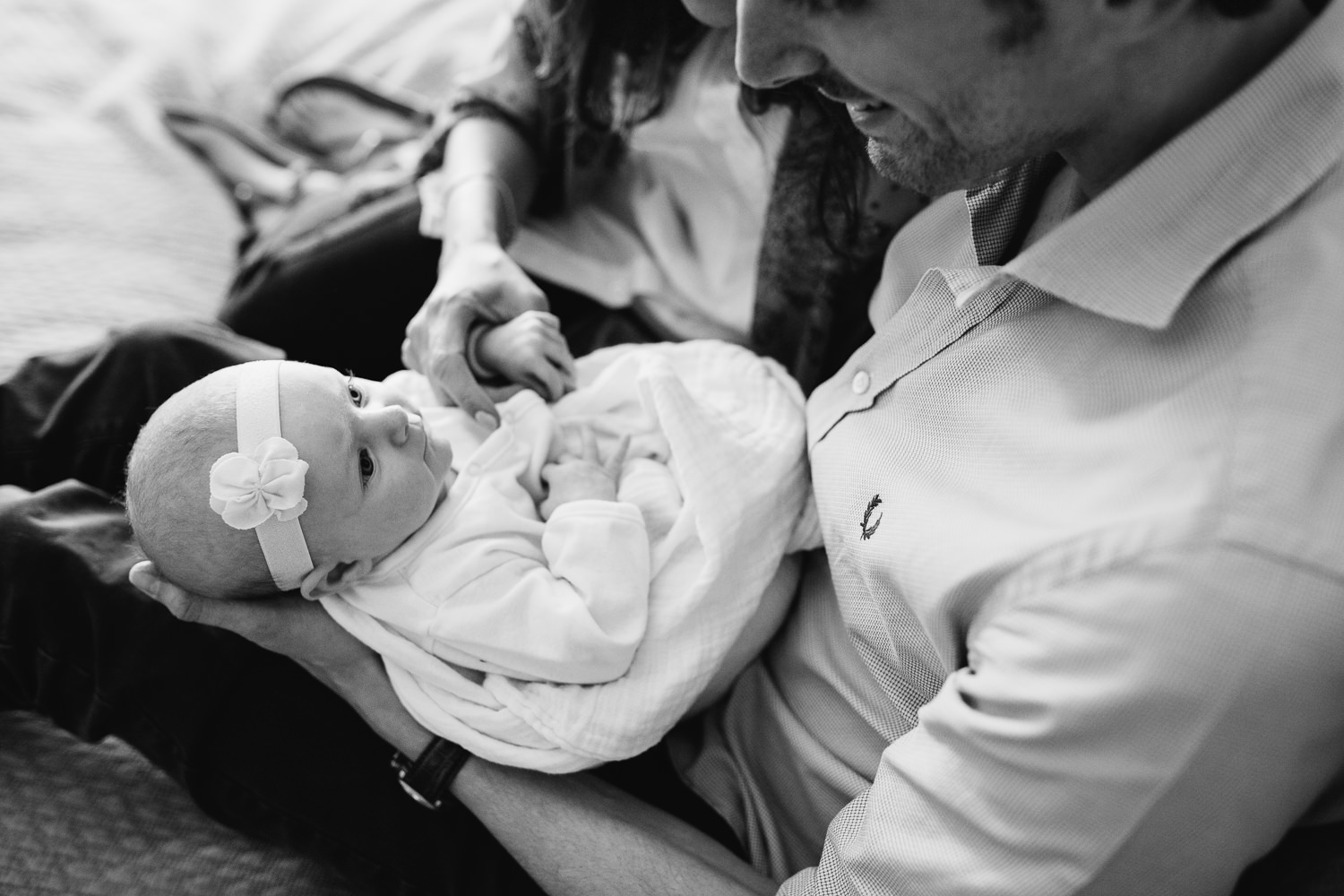 husband and wife sitting on master bed, 2 month old baby girl looking at father - Barrie In-Home Photography