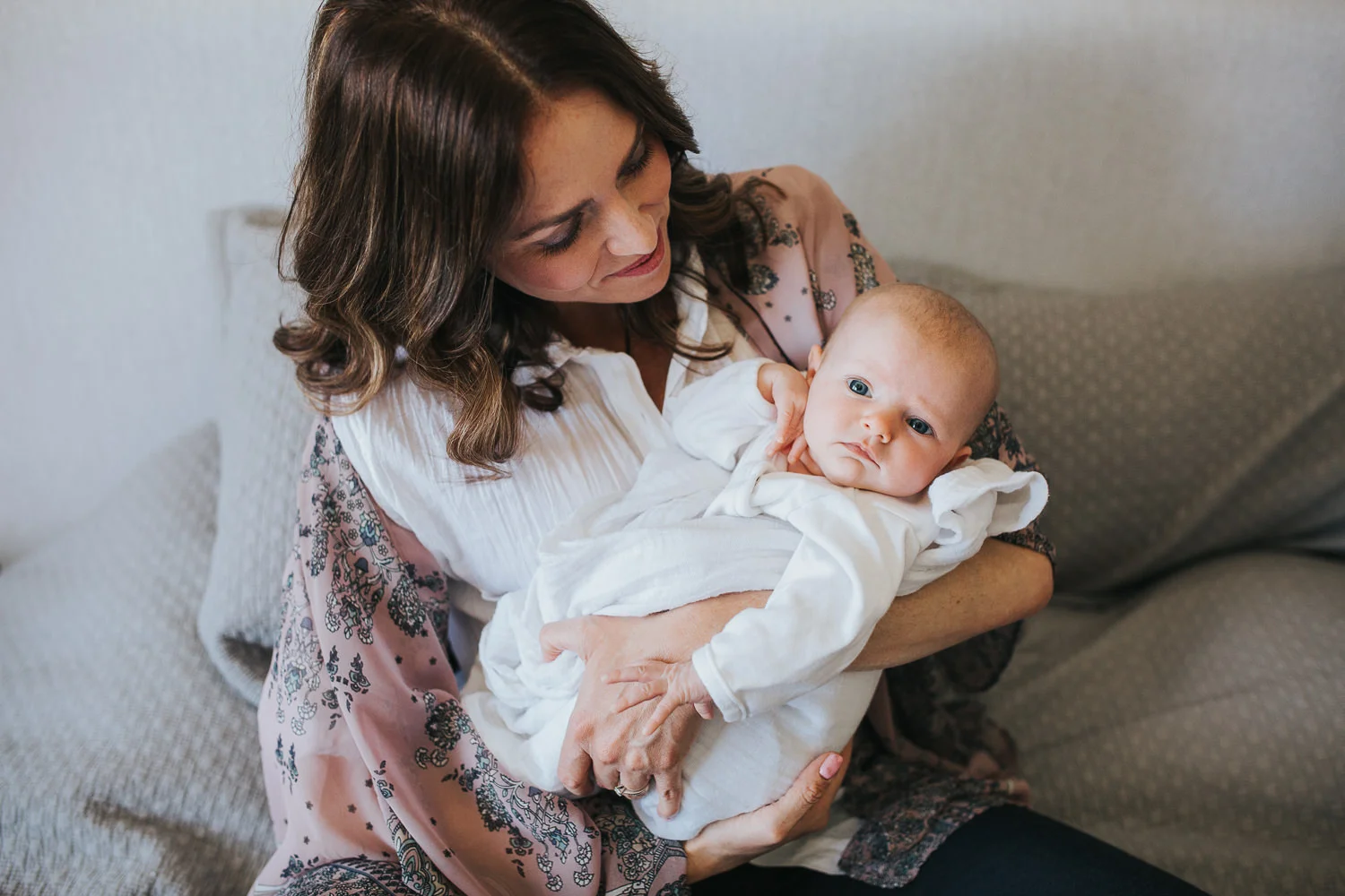 new mom sitting on bed holding 2 month old baby girl, who is looking at camera - Stouffville In-Home Photos