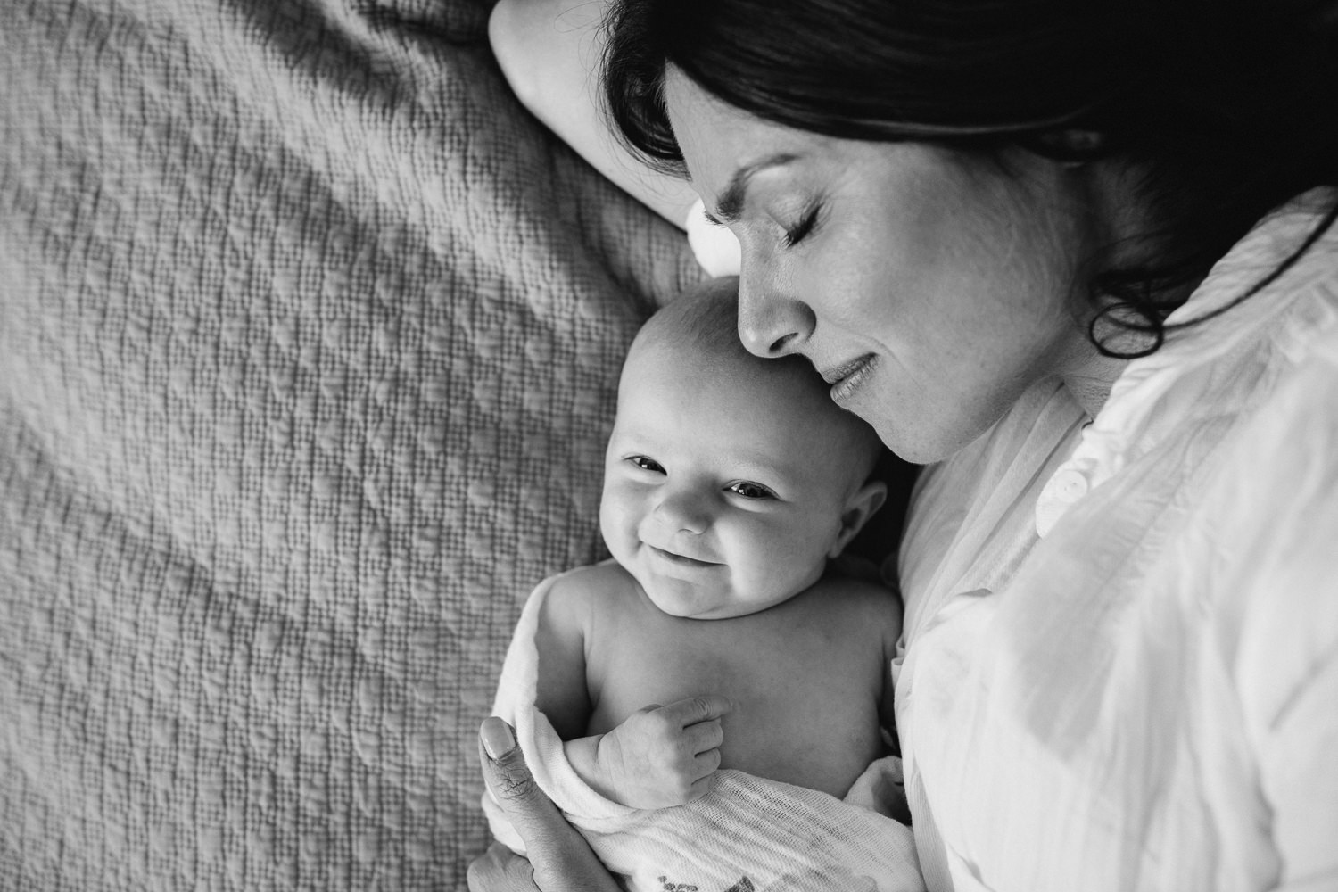 new mother lying on bed snuggling daughter, 2 month old baby girl smiling at camera - Stouffville Lifestyle Photography