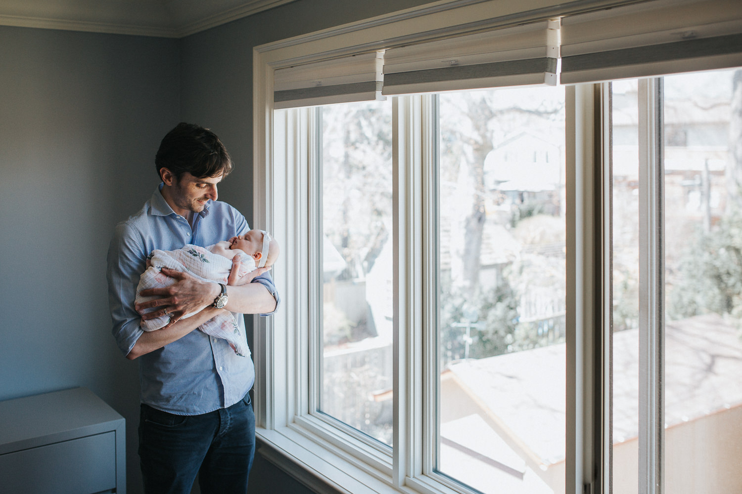 new father standing at window holding 2 month old baby girl in arms - Barrie In-Home Photography