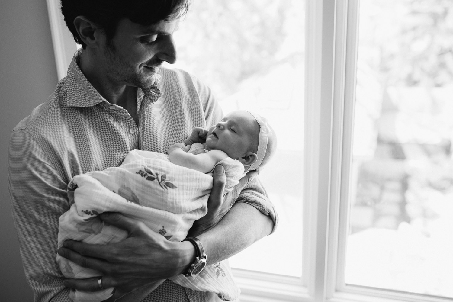 first time dad standing at window holding 2 month old baby girl in arms -Uxbridge In-Home Photography