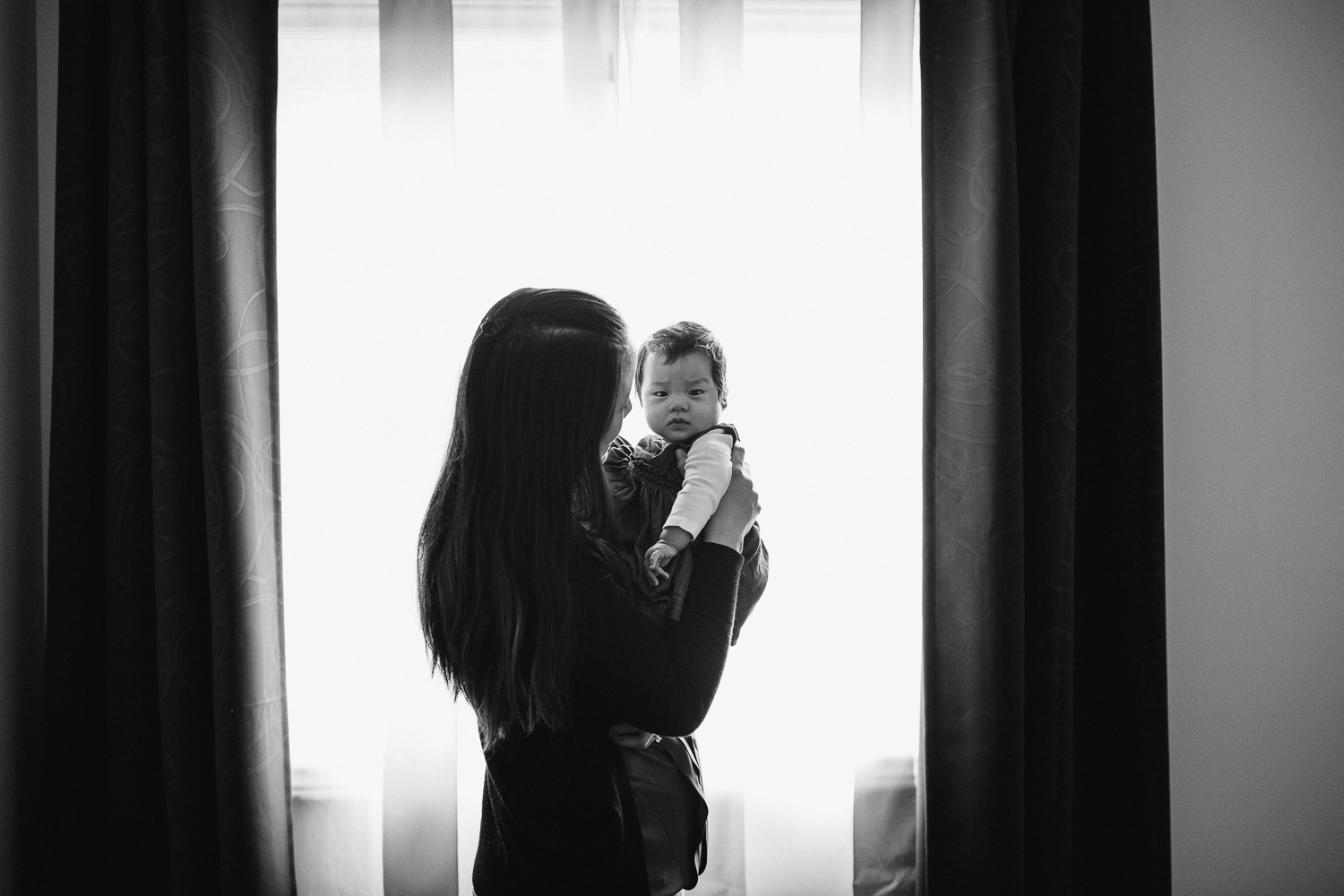 first time mom standing on front of window holding 3 month old baby daughter - Uxbridge In-Home Photography