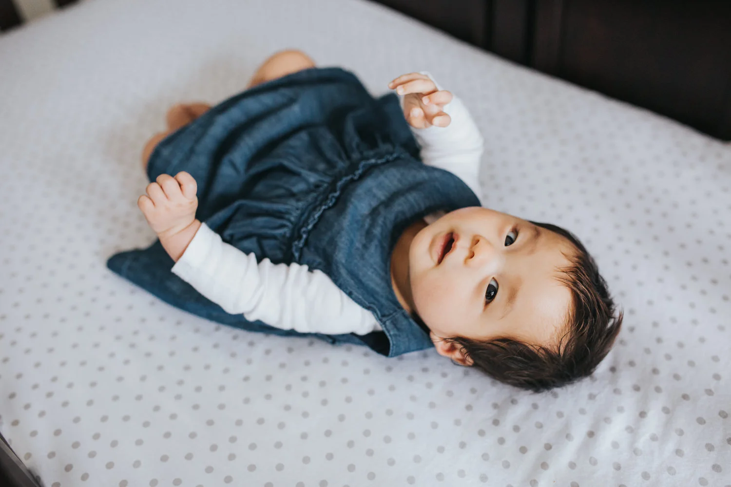 3 month old baby girl in blue dress lying in nursery crib, looking at camera - Markham Lifestyle Photography