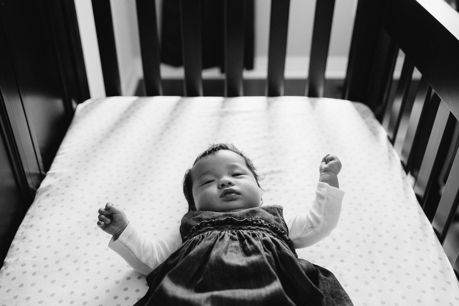 3 month old baby girl in blue dress lying in nursery crib, looking at camera - Barrie Lifestyle Photography