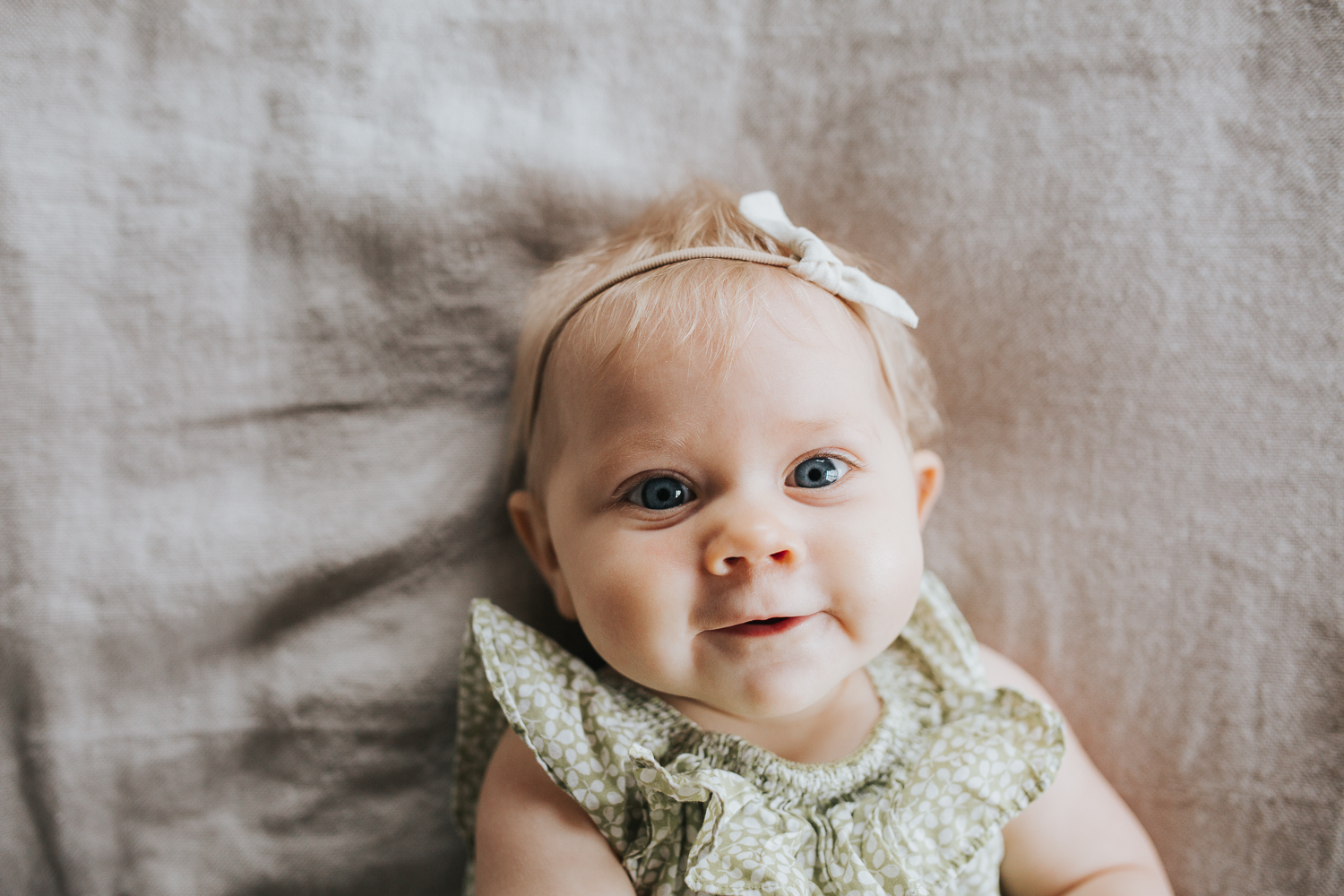 6 month old baby girl with blonde hair and blue eyes lying on bed looking at camera - Stouffville Family Lifestyle Photography