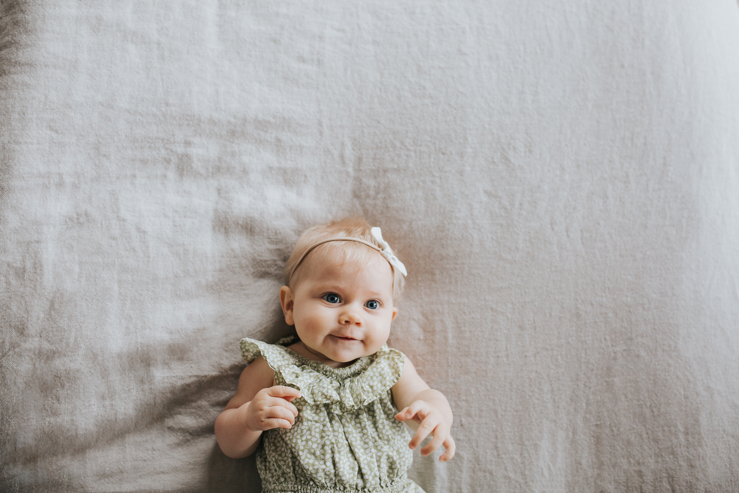 6 month old baby girl with blonde hair and blue eyes lying on bed - Newmarket Family Lifestyle Photography