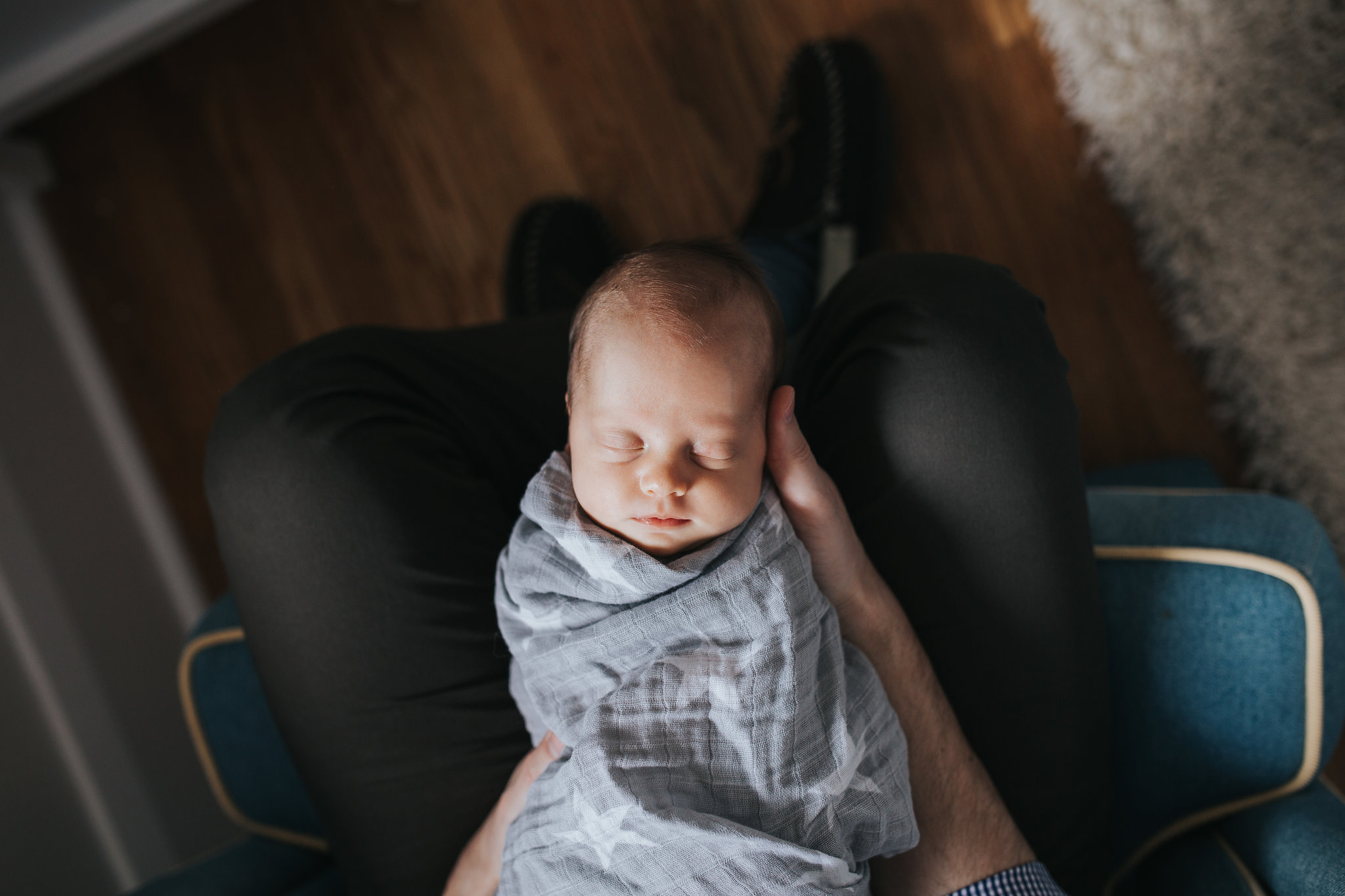 shot from above of baby girl in grey swaddle lying in her father's lap - Markham Lifestyle Photography