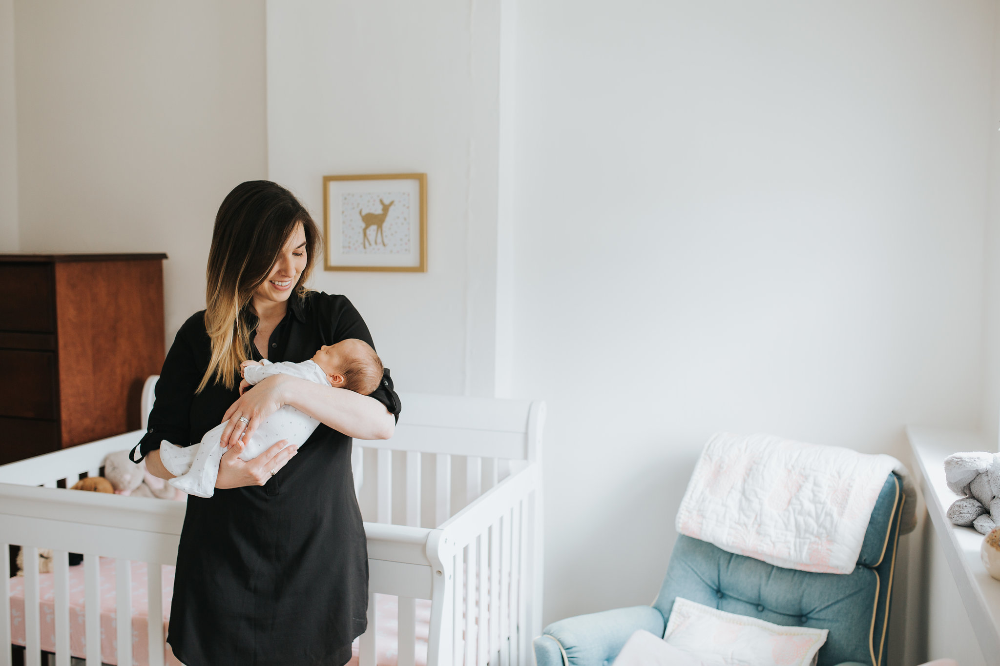 new mom holds 4 week old baby daughter standing in front of crib in pink and gold nursery - Stouffville Lifestyle Photos