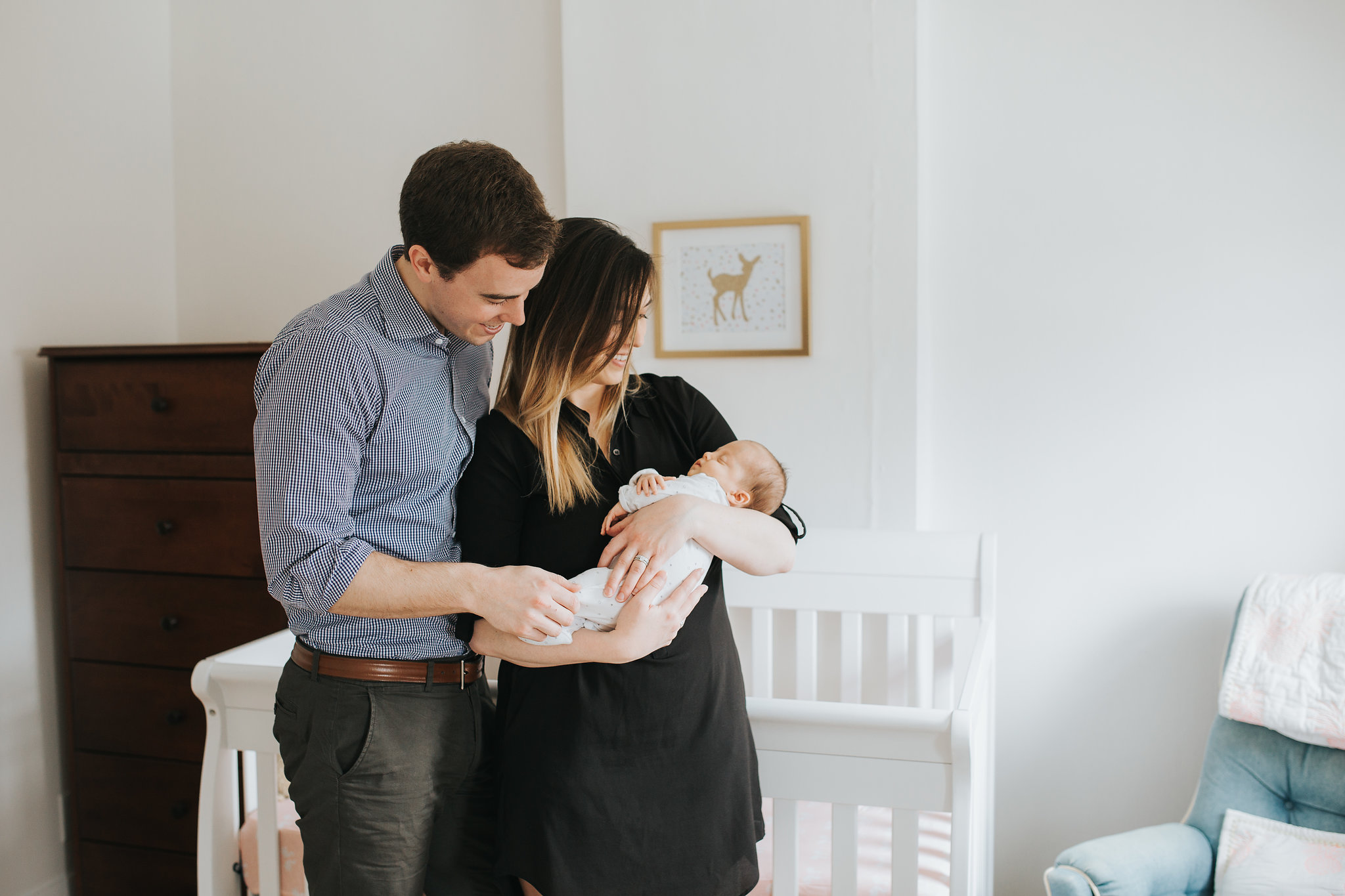 new parents hold 4 week old baby girl standing in front of crib in pink and gold nursery - Newmarket Lifestyle Photography