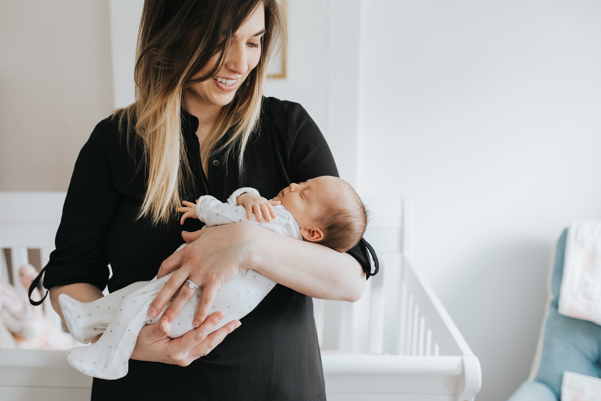 new mom holds 4 week old baby daughter standing in front of crib in pink and gold nursery - Barrie Lifestyle Photos