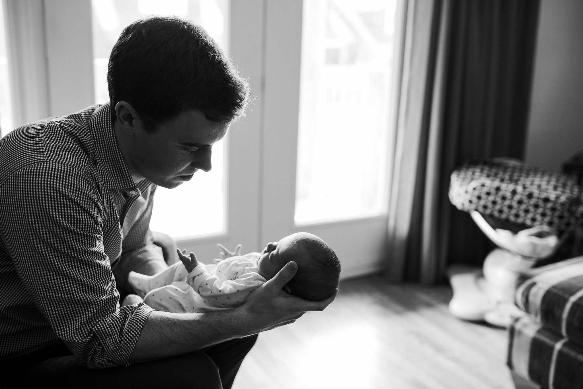 first time dad sitting in chair holding and looking at 4 week old baby girl in sleeper - Stouffville In-Home Photography