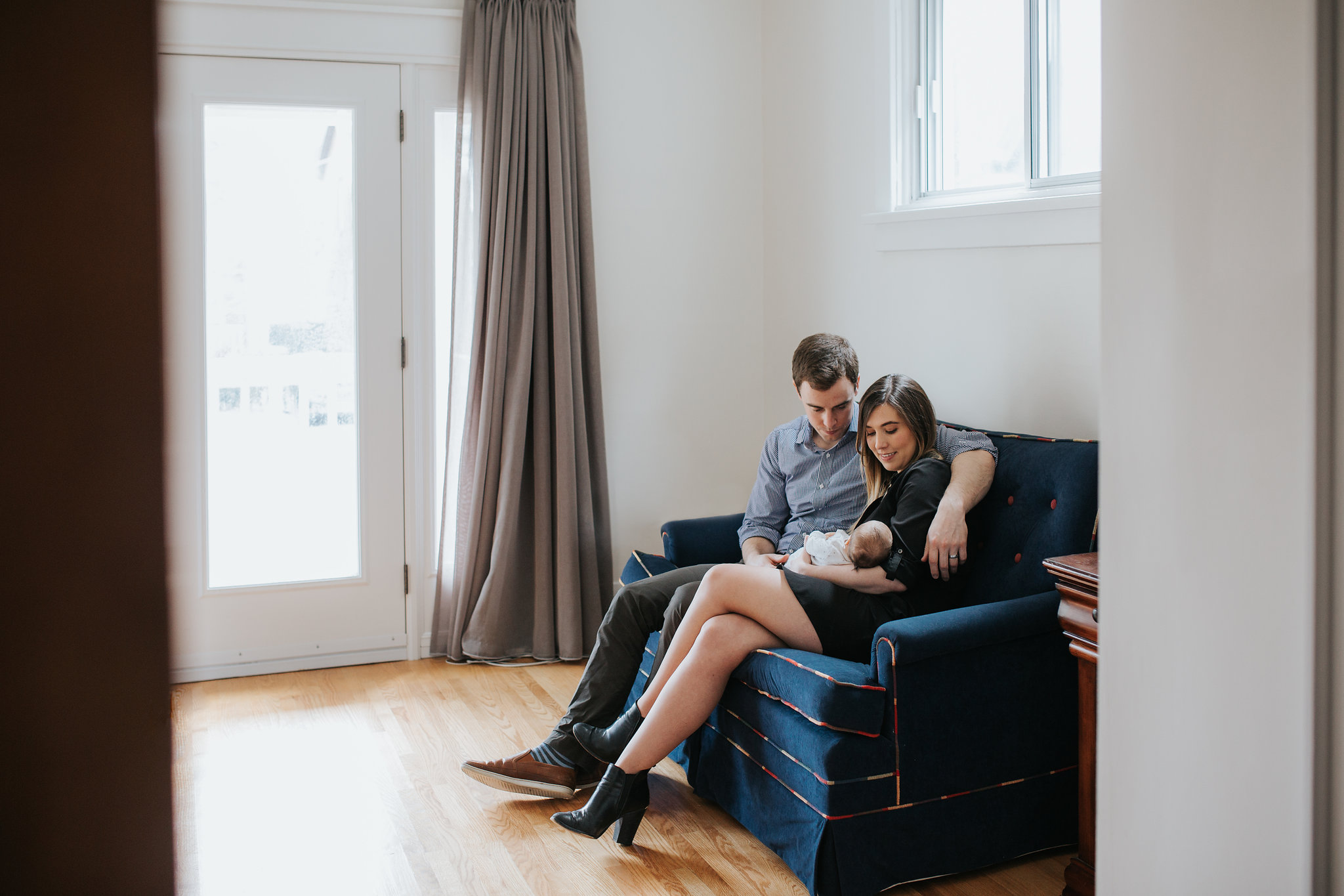 new parents sit on couch holding and looking at 4 week old baby daughter - Barrie In-Home Photography