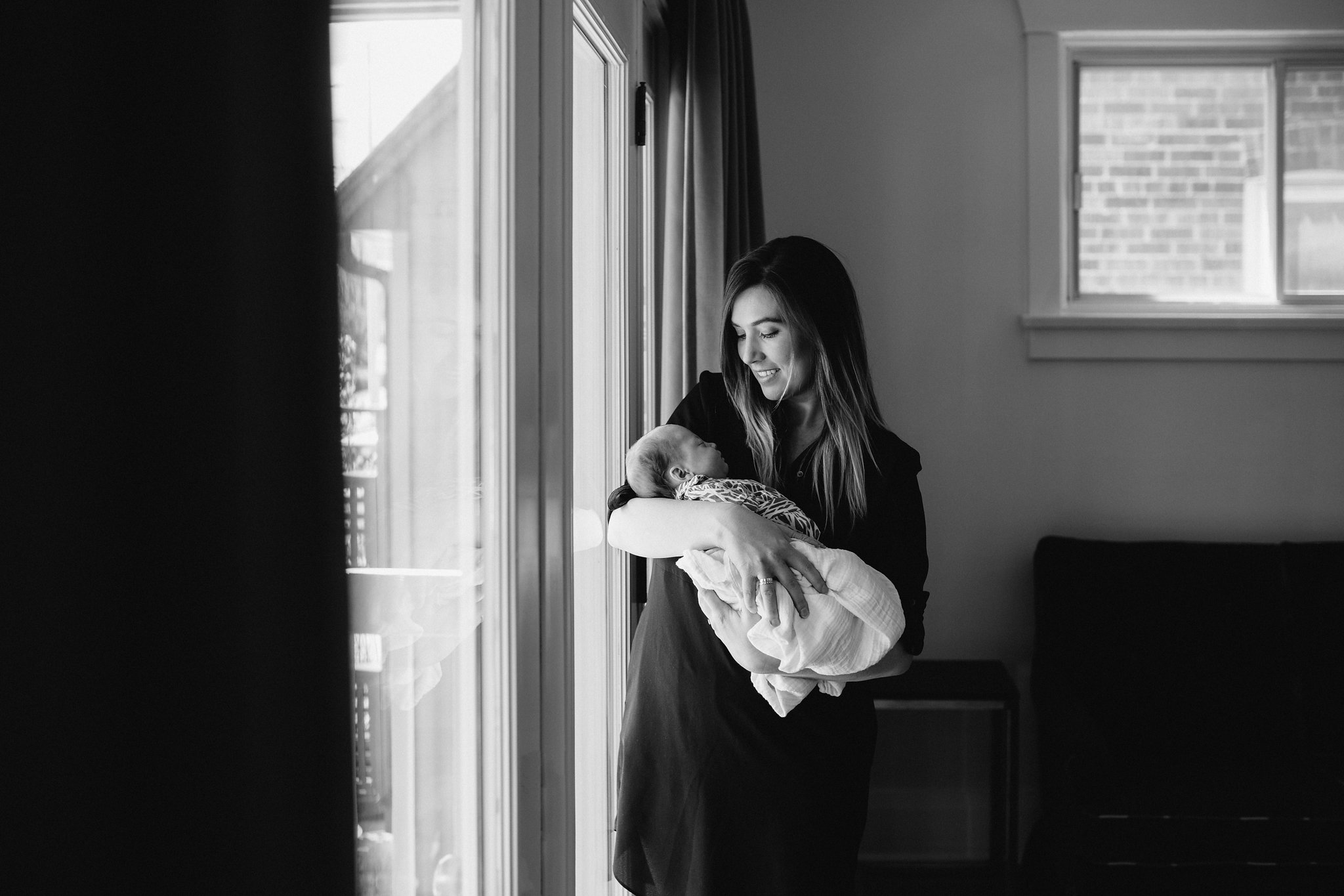 first time mom standing at window holding and looking at 4 week old baby daughter - Newmarket Lifestyle Photos