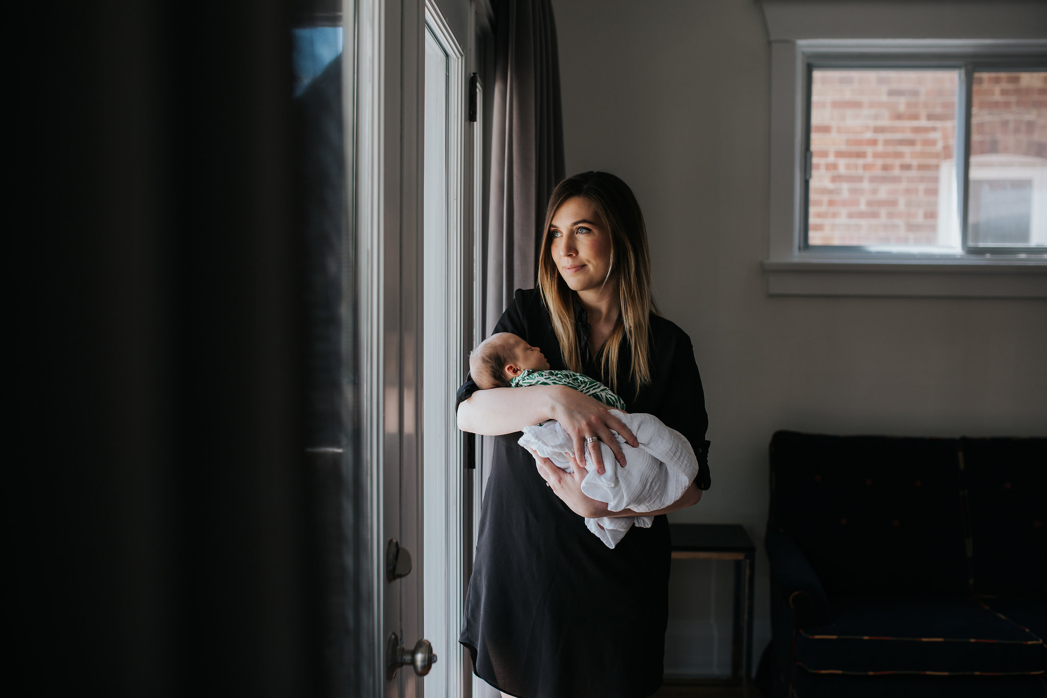 first time mom standing at window holding and looking at 4 week old baby daughter - Stouffville Lifestyle Photos
