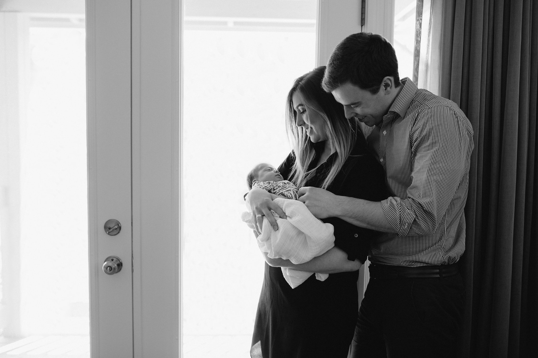 new parents standing at window holding and looking at 4 week old baby girl - Markham Lifestyle Photos
