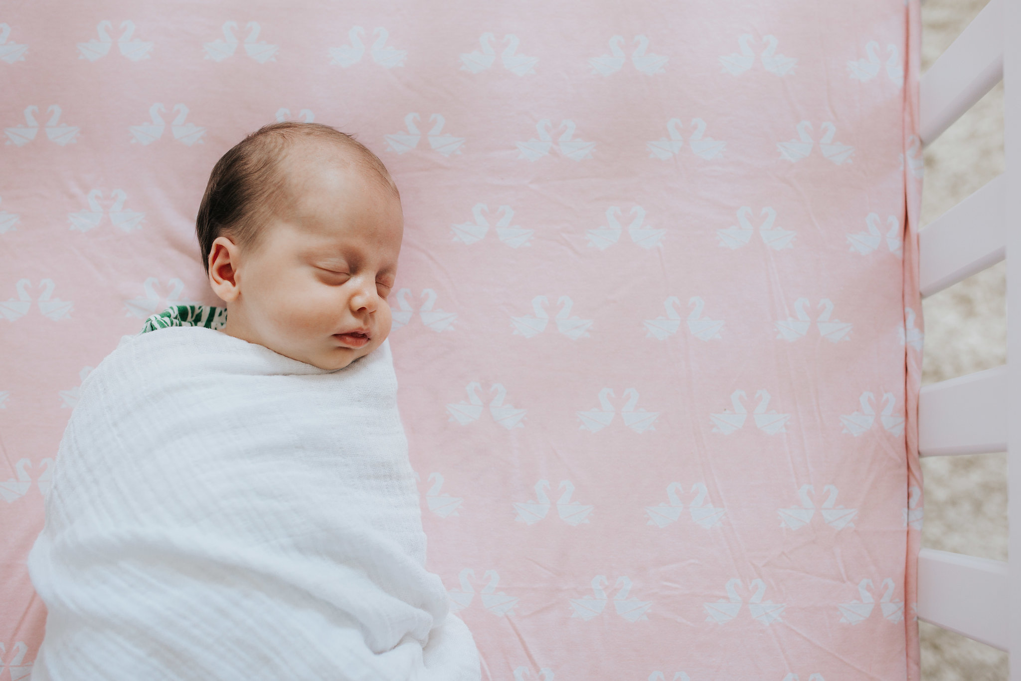 4 week old baby girl in white swaddle sleeping in crib with pink sheets - Barrie Lifestyle Photography