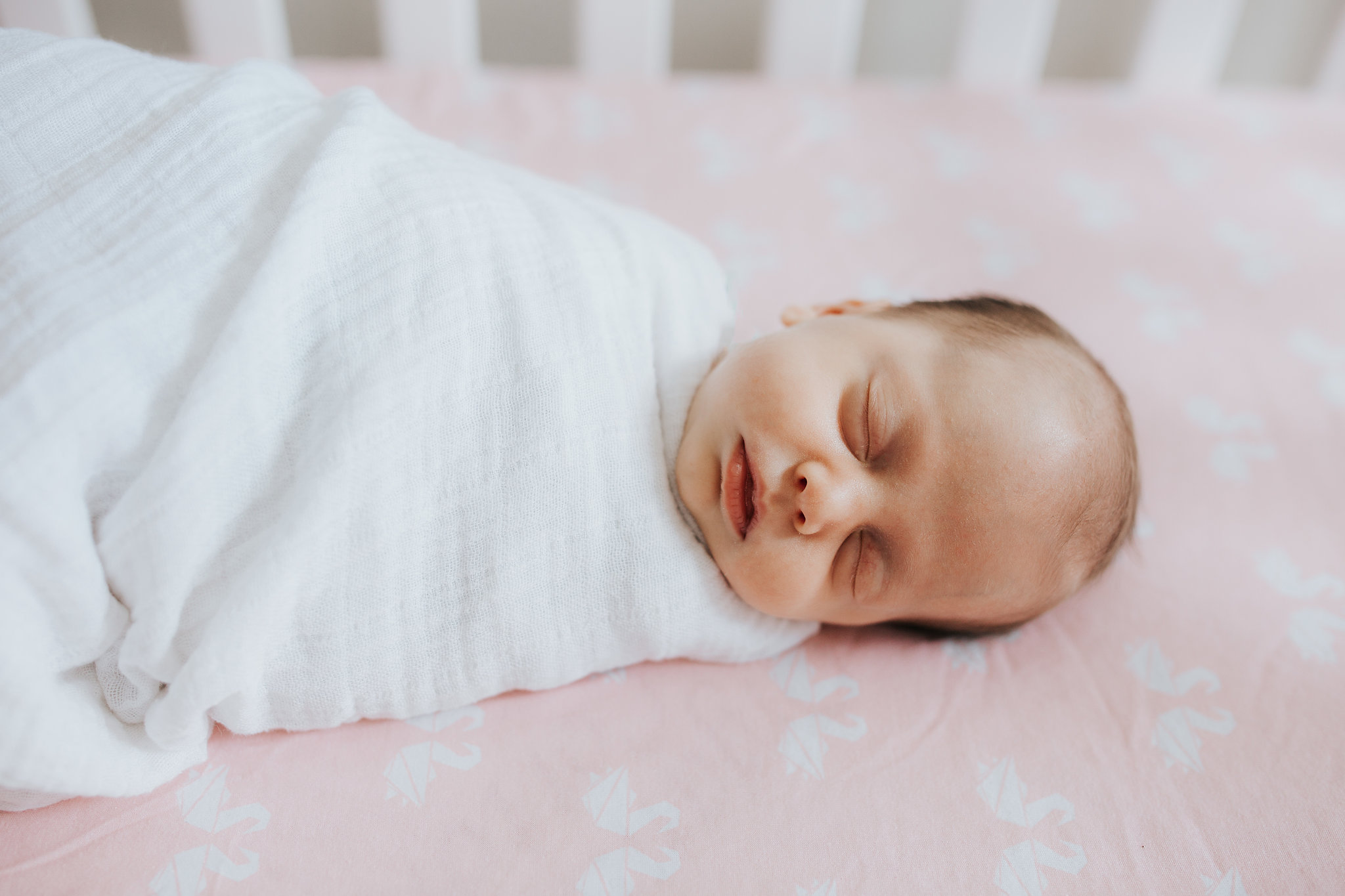 4 week old baby girl in white swaddle sleeping in crib with pink sheets - Newmarket Lifestyle Photography