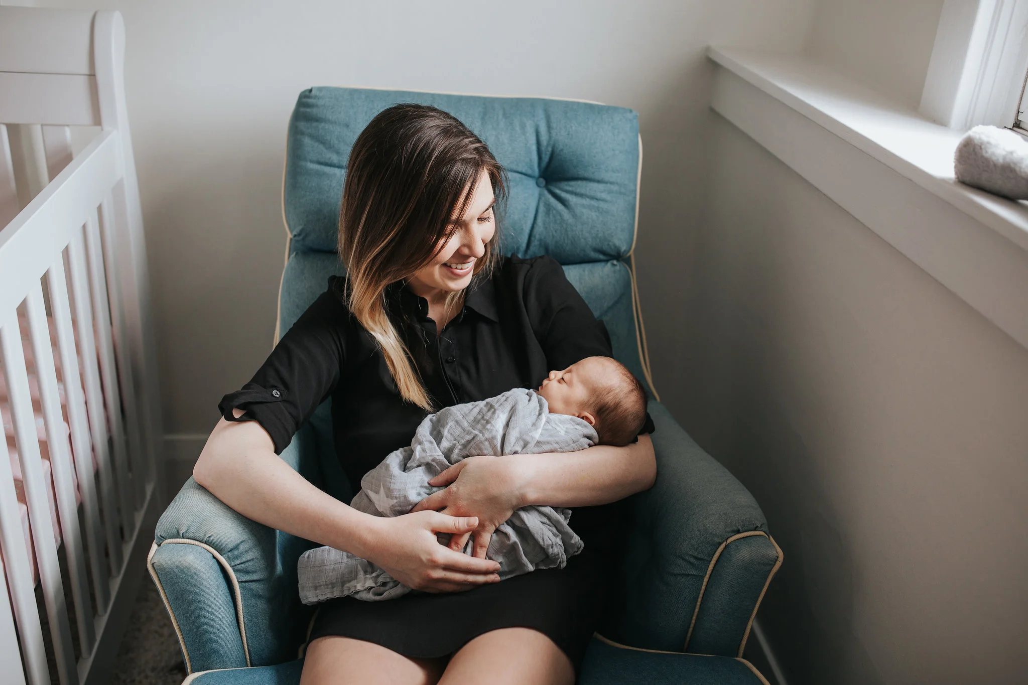 first time mom sits in chair holding and smiling at baby girl - Newmarket Lifestyle Photography