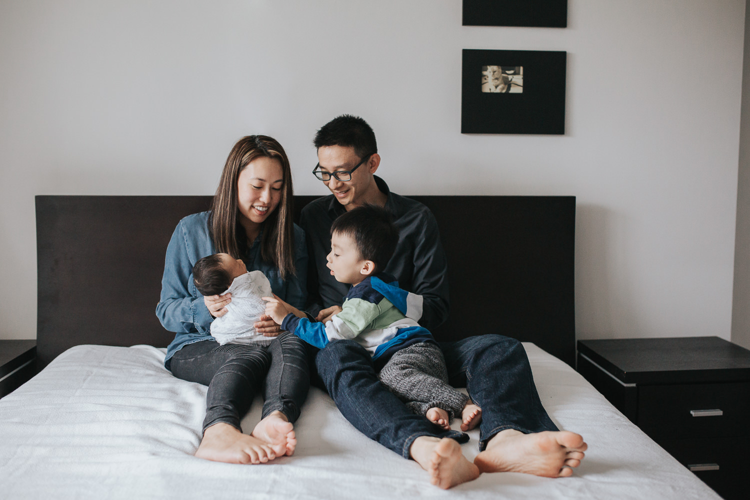 Family of 4 with 2 year old toddler boy and 2 week old baby son sitting on bed - Newmarket In-Home Photos