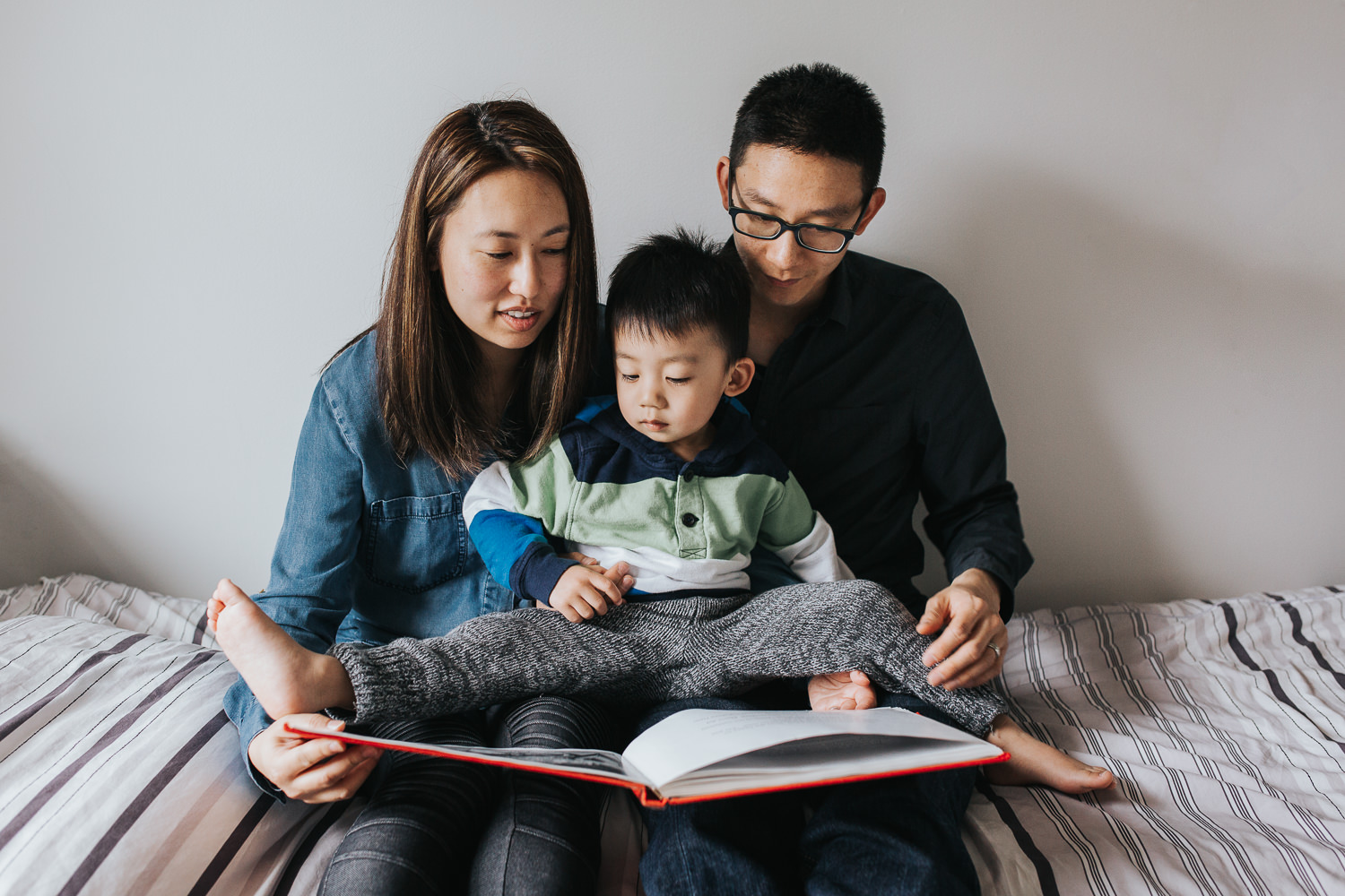 mom and dad sitting on bed reading story to 2 year old toddler boy - Markham Lifestyle Photos