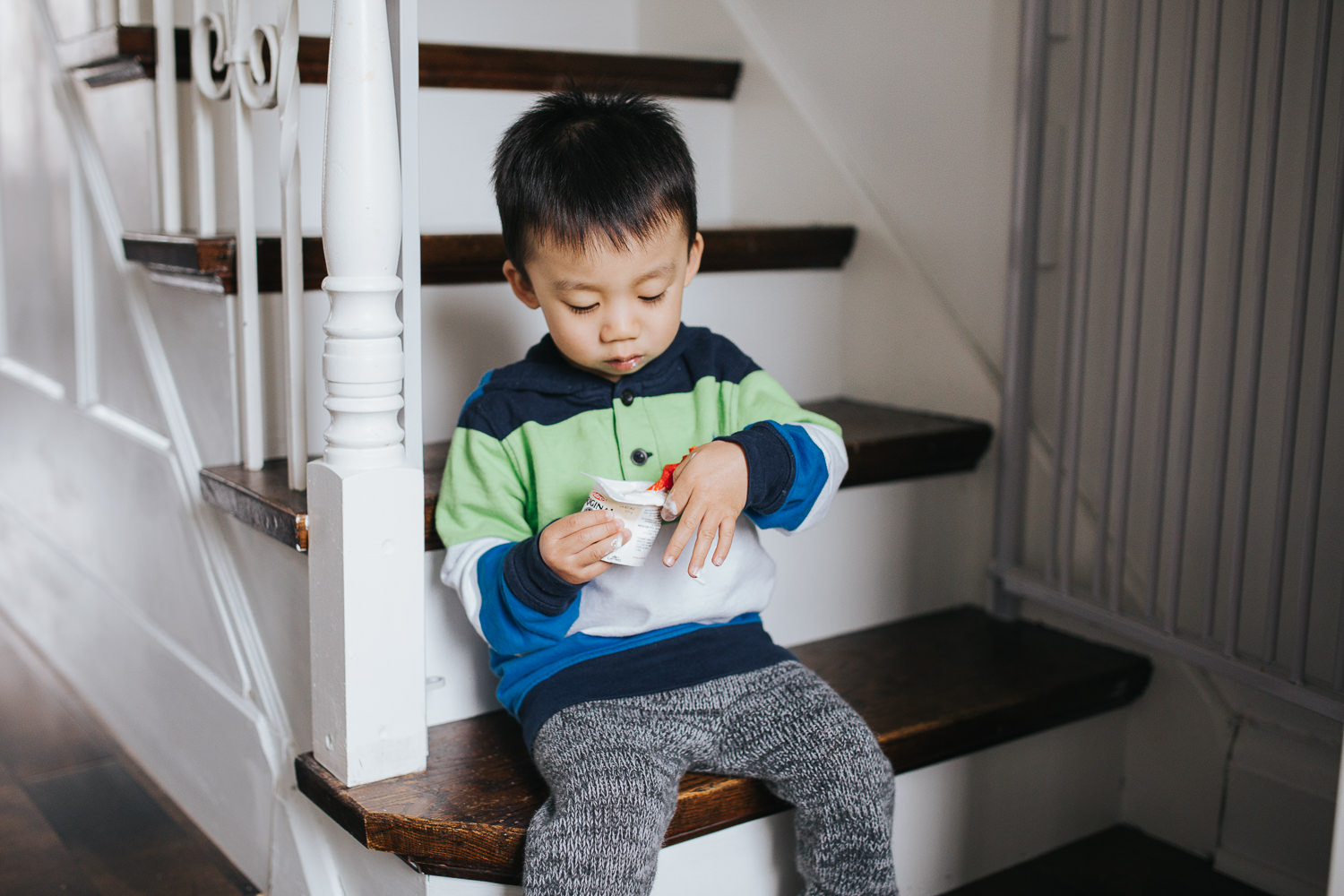 2 year old toddler boy sitting on stairs eating yogurt - Markham Lifestyle Photography