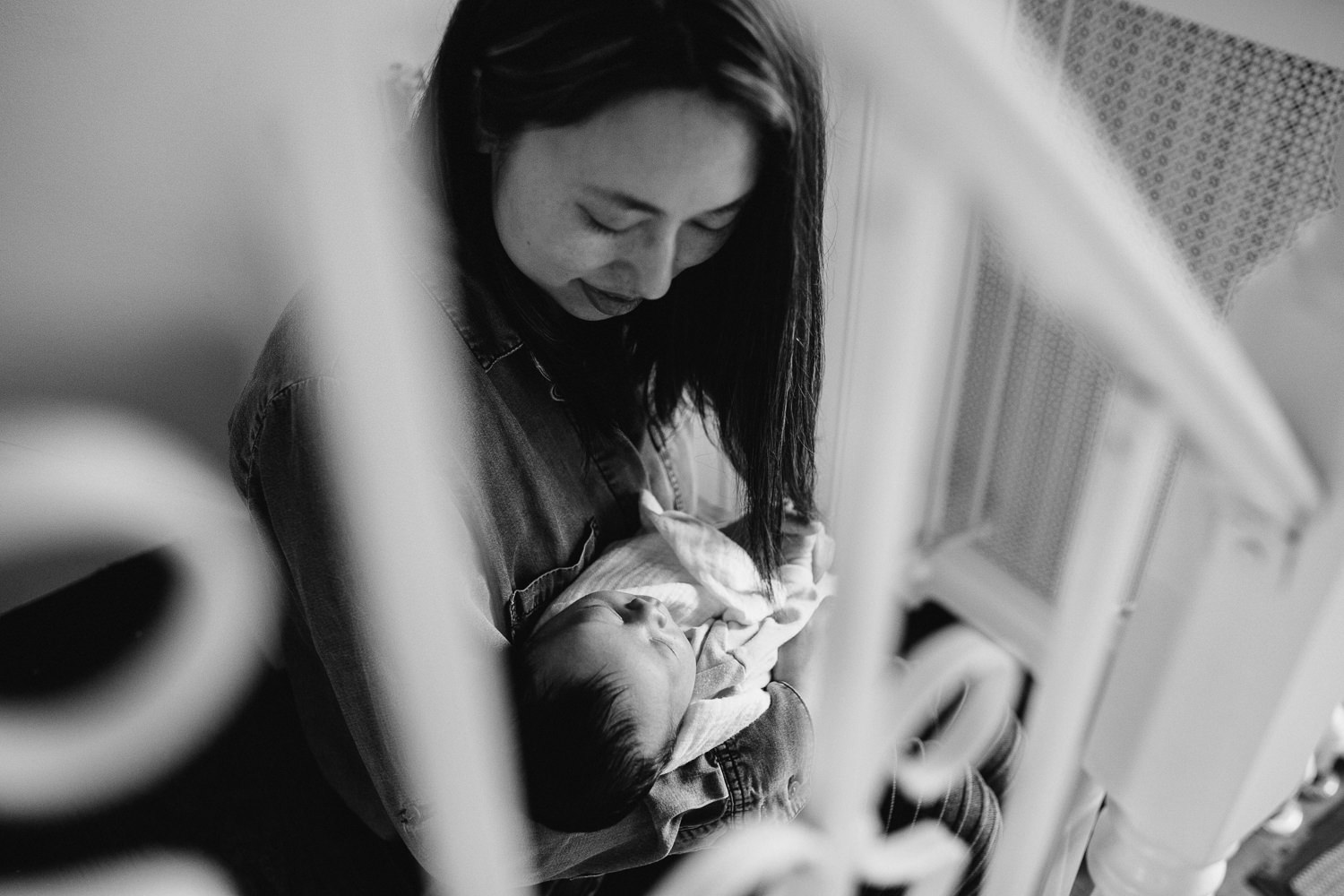 mom with dark hair sits on stairs holding 2 week old baby boy - Newmarket In-Home Photography