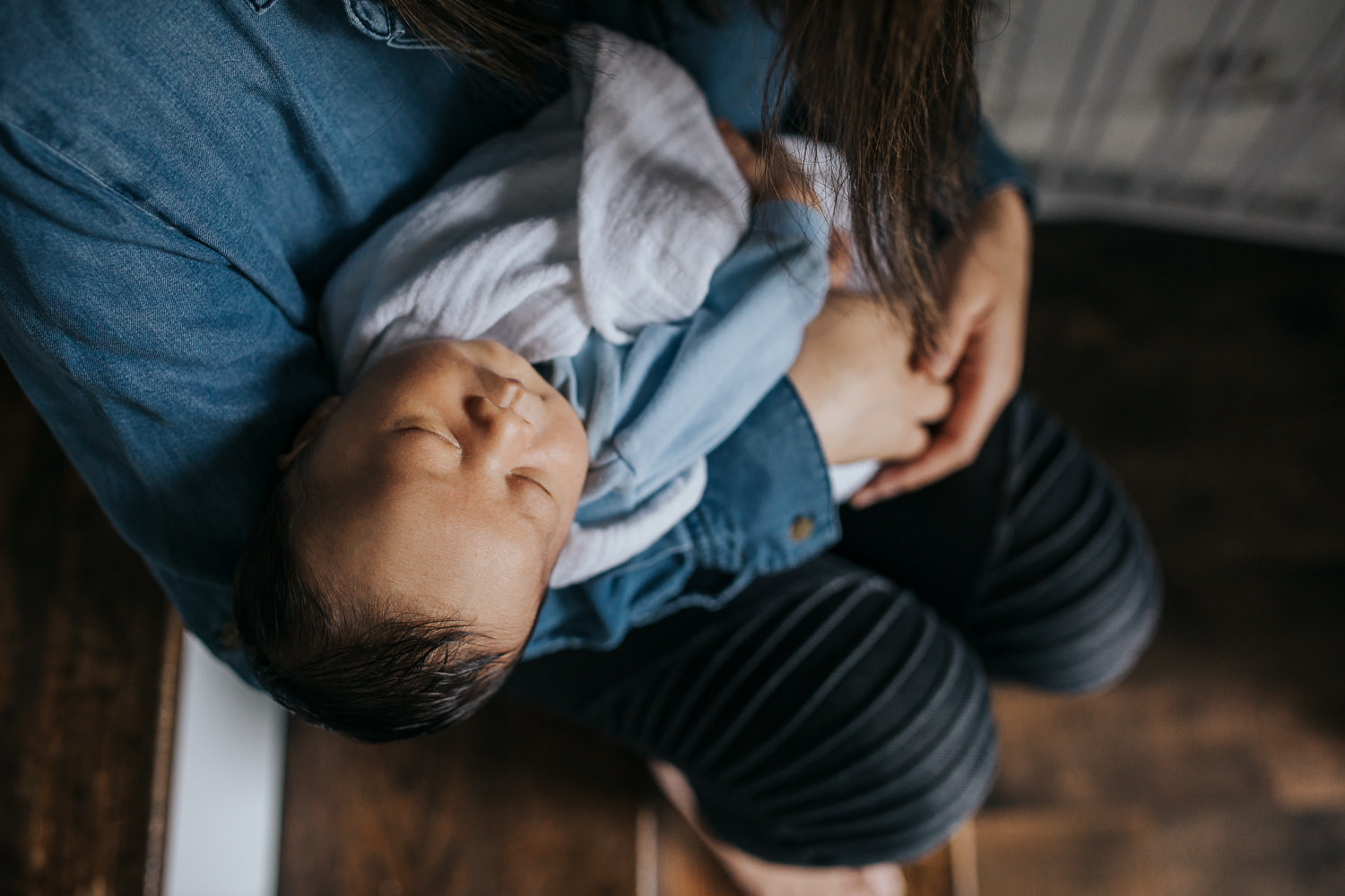 mom in blue shirt with dark hair sits on stairs holding 2 week old baby boy - Markham In-Home Photography