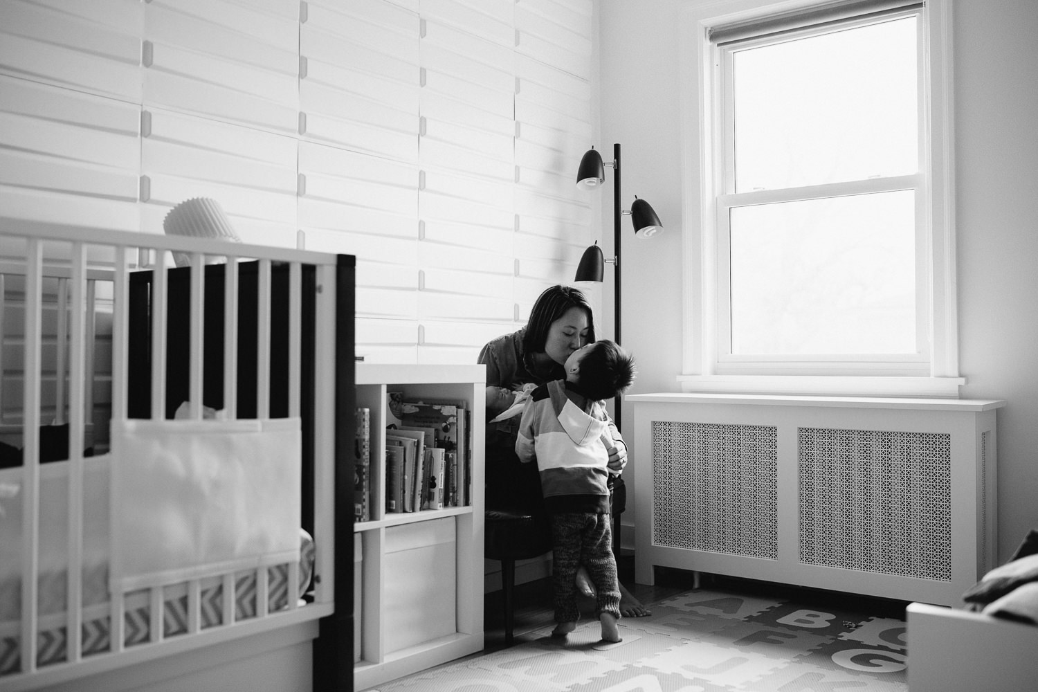 2 year old toddler boy kisses mom who is sitting holding 2 week old baby boy - Newmarket In-Home Photos