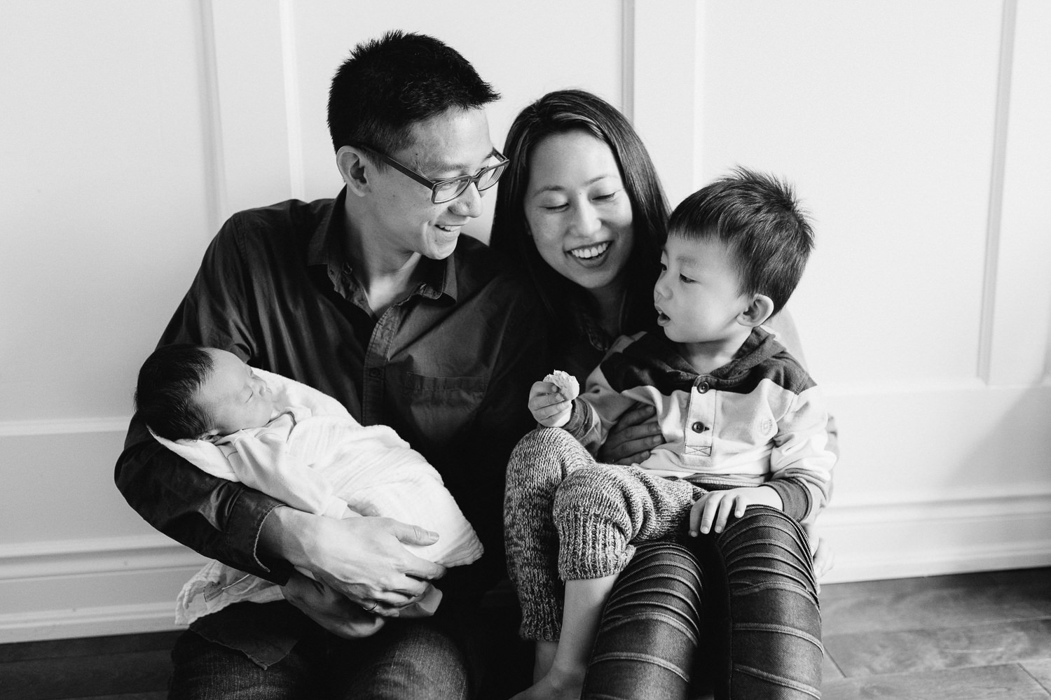 family of 4 with 2 week old boy sit on floor, looking at 2 year old toddler boy - Newmarket Lifestyle Photography