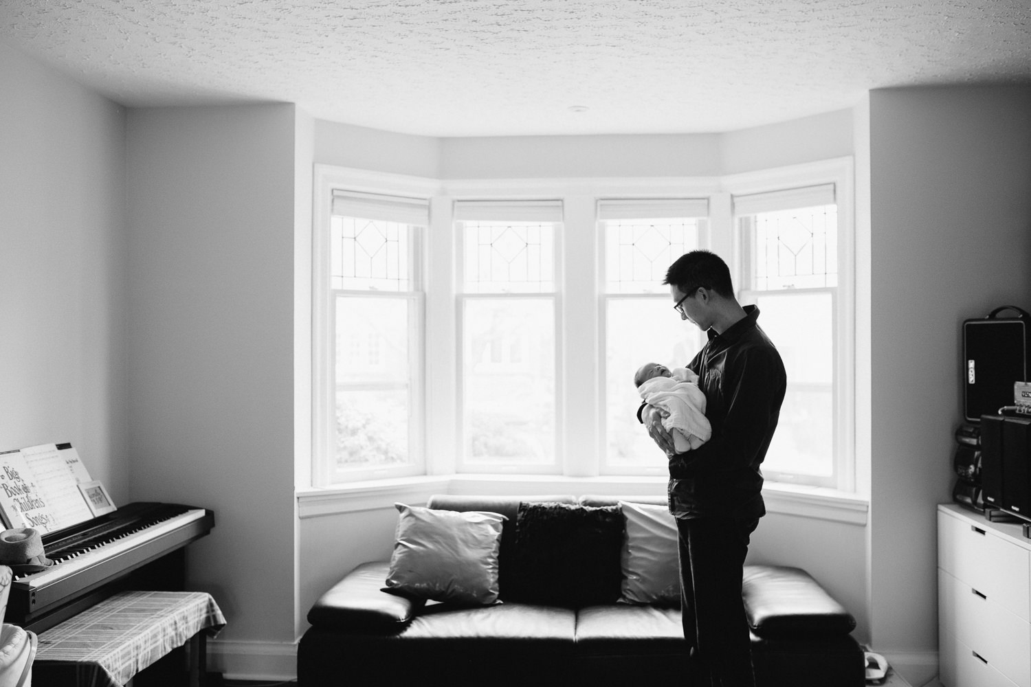 dad stands in living room holding 2 week old baby boy asleep in his arms - Newmarket Lifestyle Photos