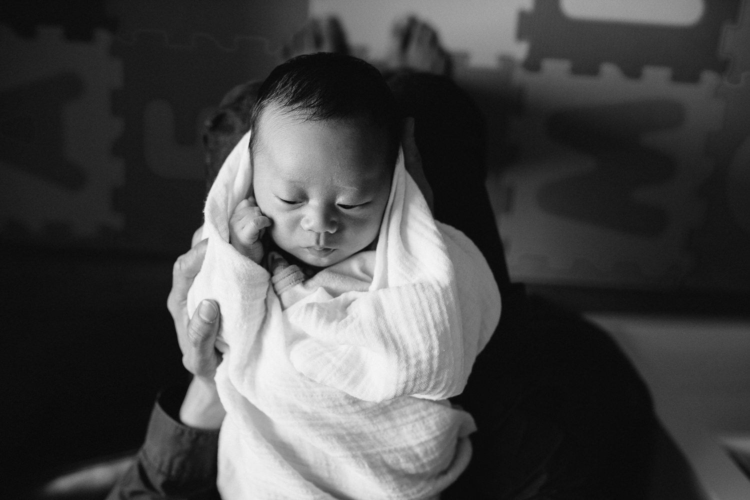 2 week old baby boy in white swaddle asleep in dad's arms, shot from above - Markham Lifestyle Photos