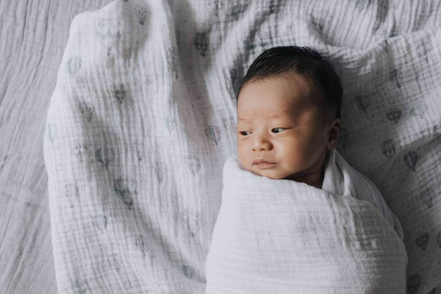 2 week old baby boy lying on bed in white swaddle - Markham Lifestyle Photography