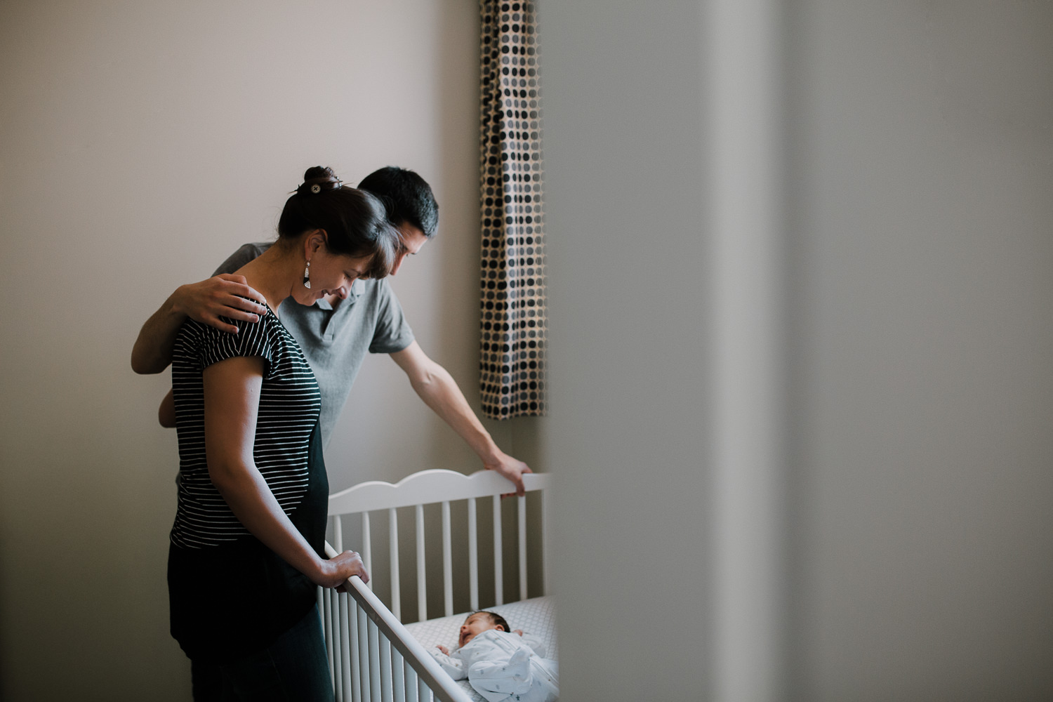 mom and dad standing over crib looking at 2 week old baby daughter sleeping inside - Markham In-Home Photography