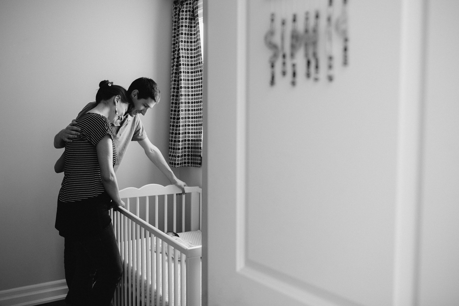 mom and dad standing over crib looking at 2 week old baby daughter sleeping inside - Barrie In-Home Photography