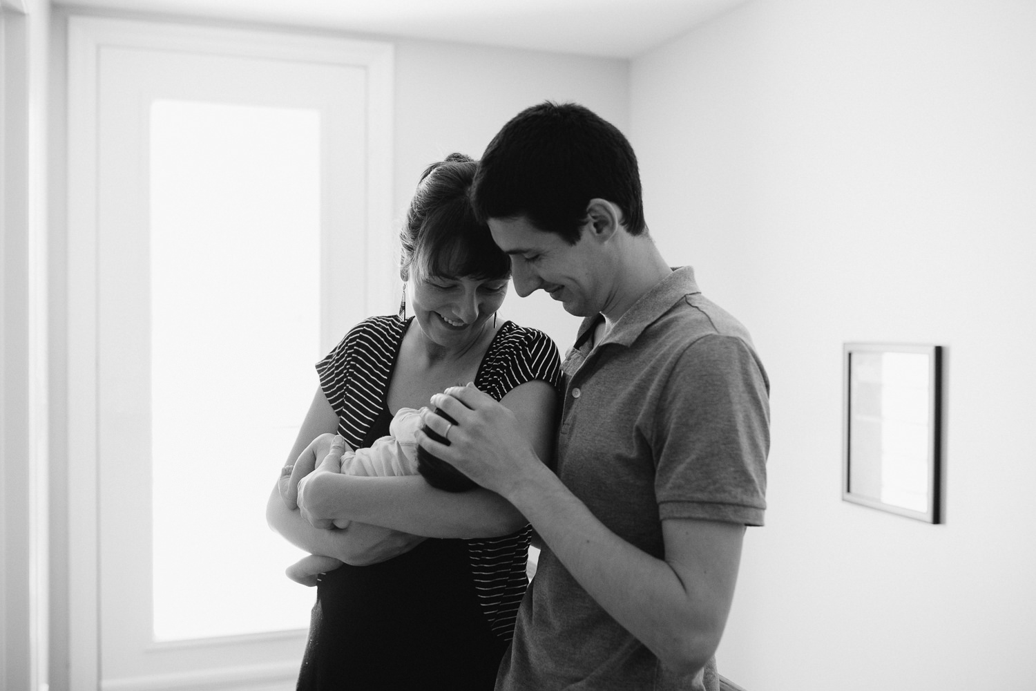 new parents snuggle and smile at 2 week old baby daughter - Newmarket In-Home Photos