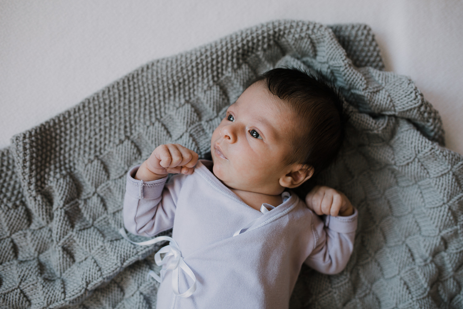 2 week old baby girl in purple onesie lying on hand knitted grey blanket - Barrie In-Home Photography